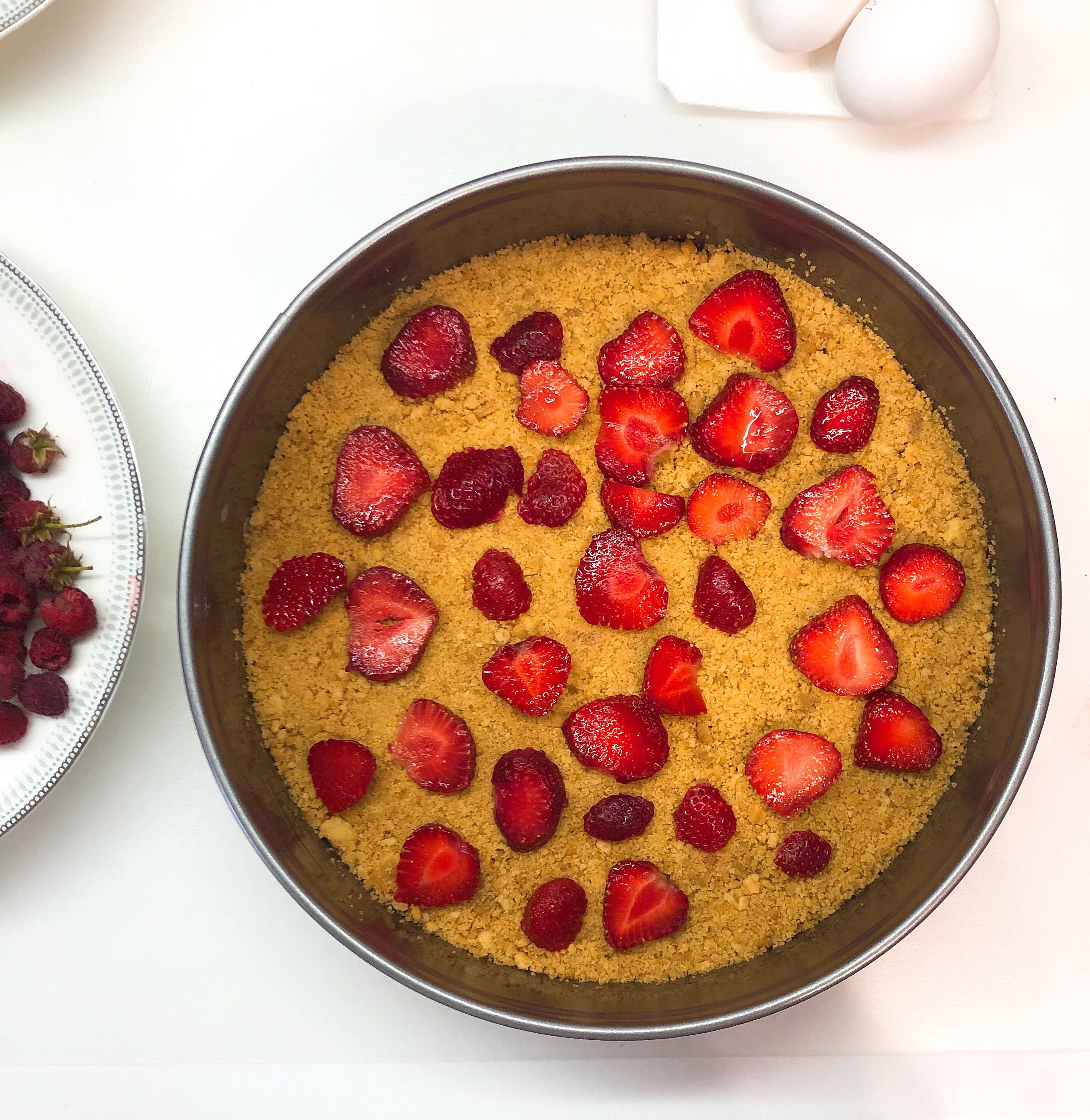 Springform pan with cookie layer and some strawberries on top